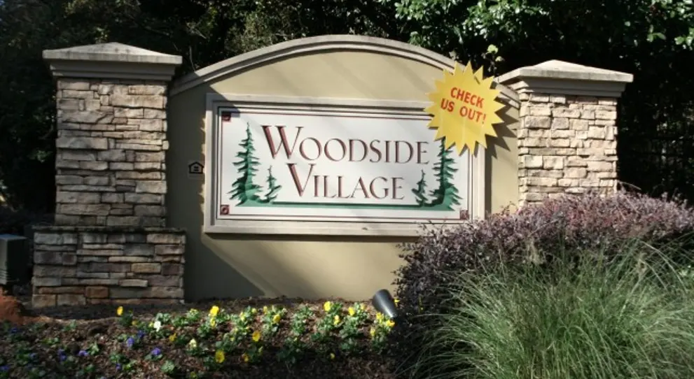Exterior sign of Woodside Village Apartments in Stone Mountain, Georgia, site of a DeKalb County shooting that left a 19-year-old critically injured, highlighting potential security concerns at residential properties.