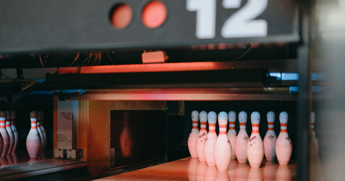 Dimly lit bowling alley lane with ten pins set up under a red glow, representing entertainment venues like Lucky Strike at Atlantic Station. 28-Year-Old Man Shot After Altercation Spills Out of Lucky Strike at Atlantic Station.