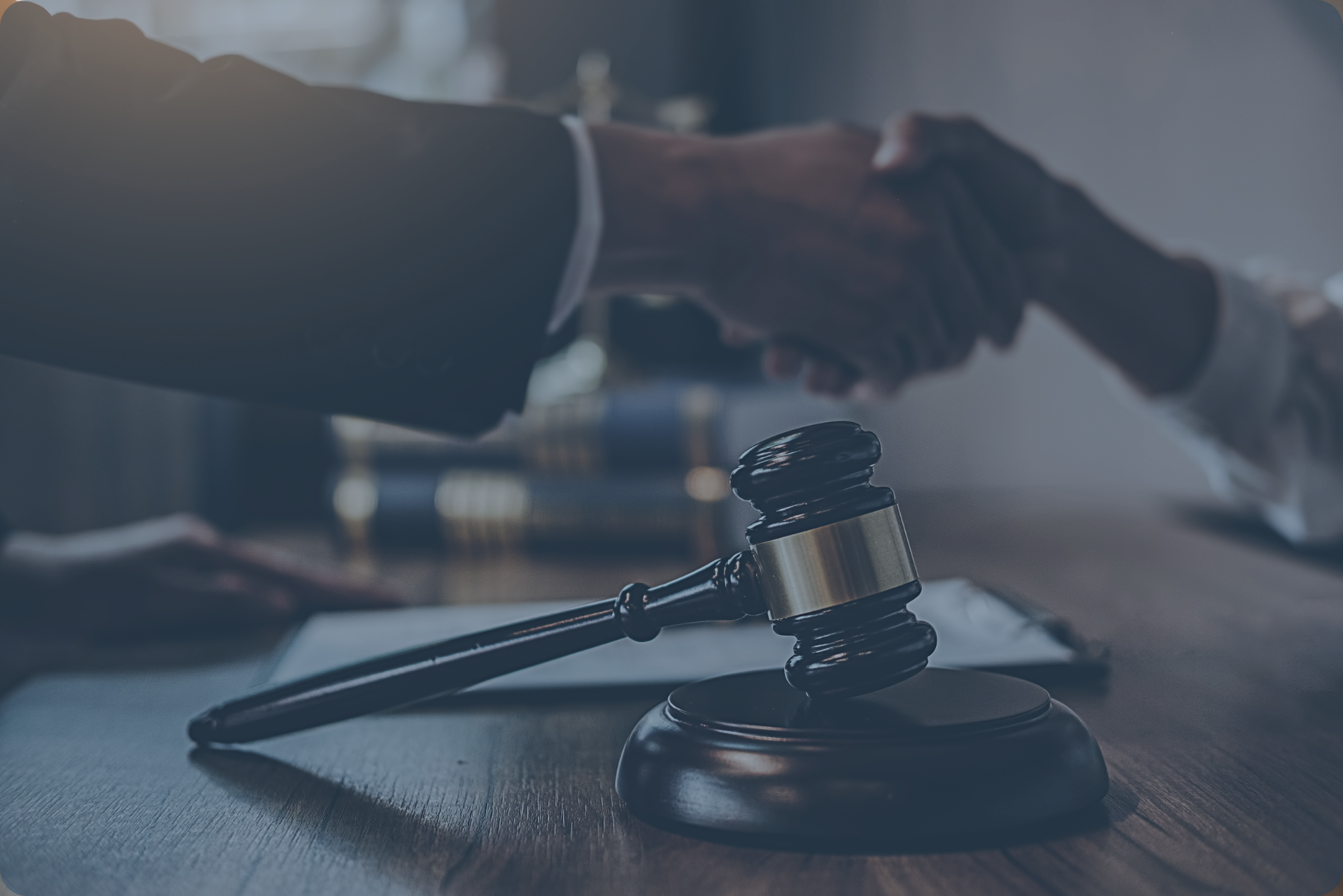 Close-up of a wooden legal gavel on a desk with a lawyer and client shaking hands in the blurred background.
