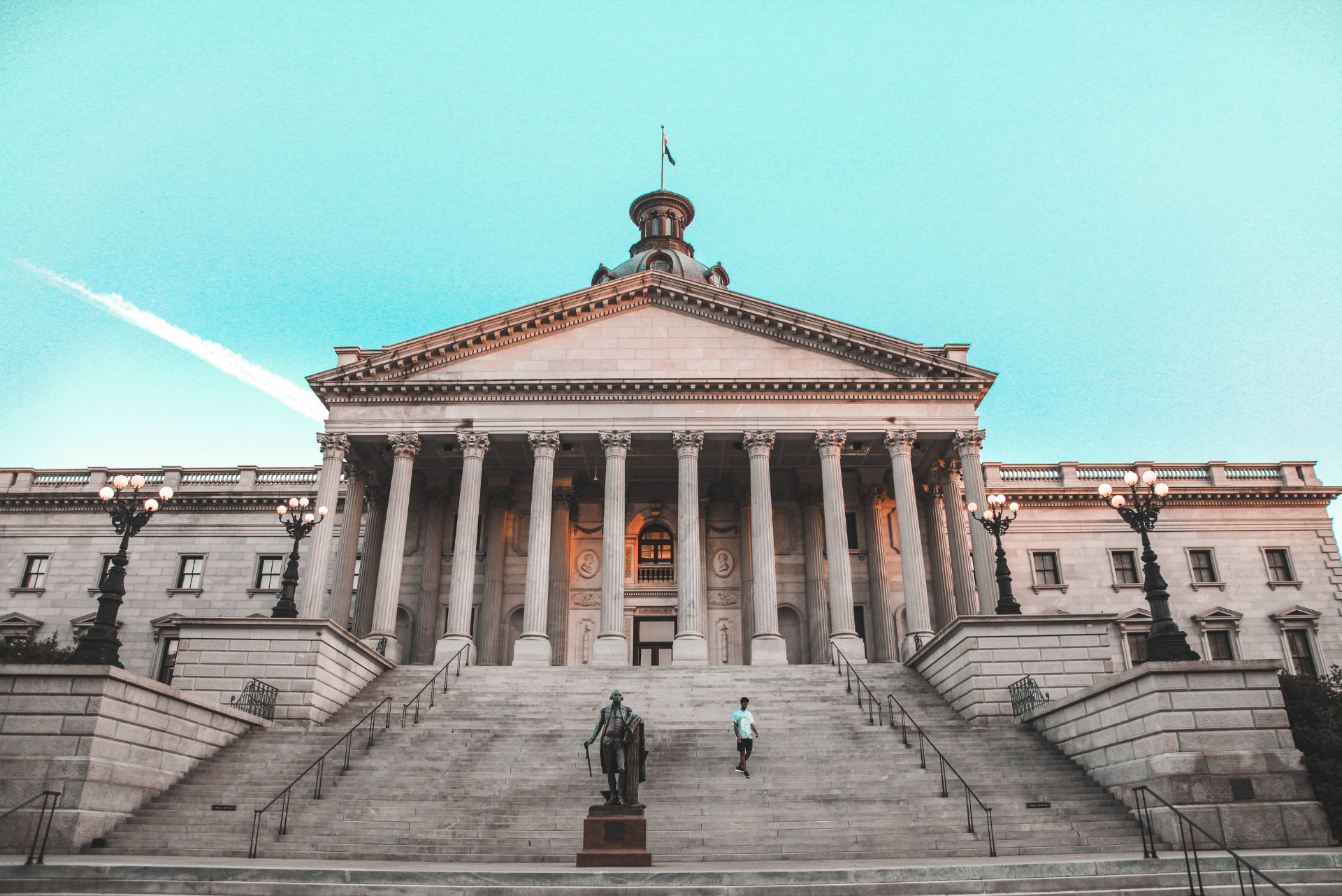 Exterior view of a South Carolina government building with a person walking down large stone steps, related to FBI Arrests Private School Teacher for Sexual Exploitation at Heathwood Hall in Columbia, SC: What Are the Legal Options for Victims and Families?